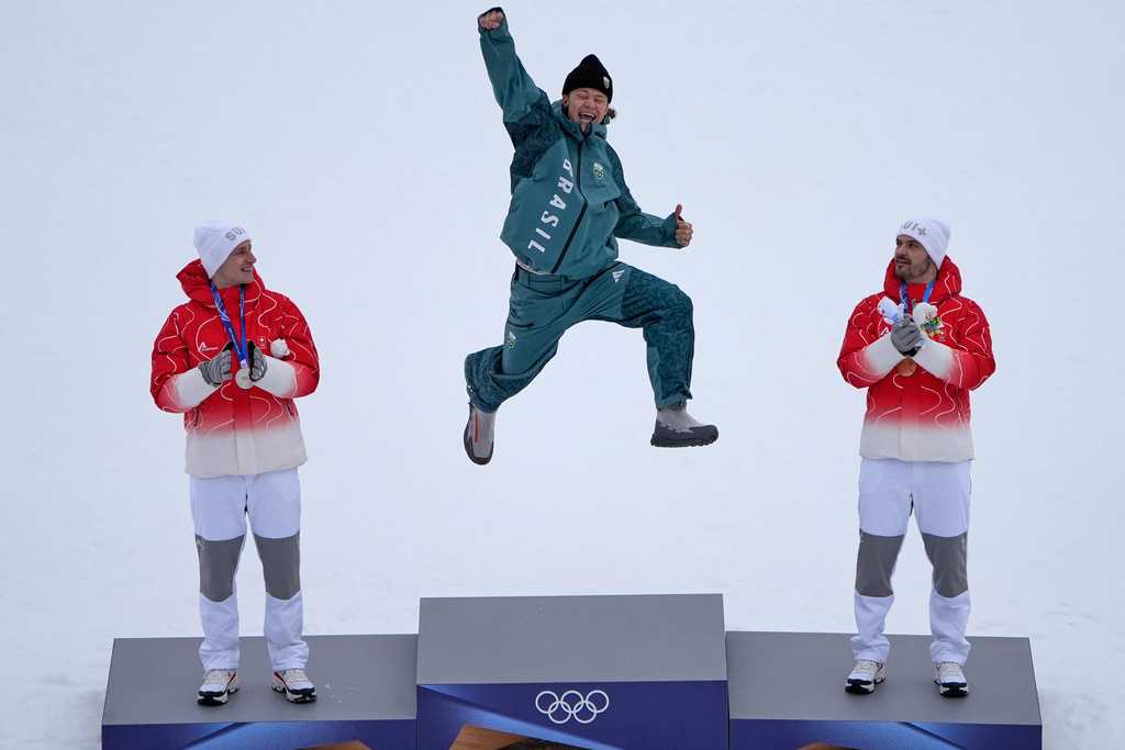 Brazil's Lucas Pinheiro Braathen, center, winner of an alpine ski, men's giant slalom race, jumps in celebration on the podium flanked by second-place Switzerland's Marco Odermatt, left, and third-place Switzerland's Loic Meillard, at the 2026 Winter Olympics, in Bormio, Italy, Feb. 14, 2026.