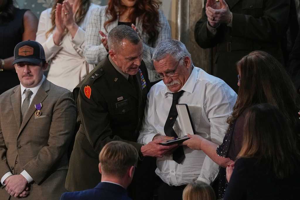 Evalea and Gary Beckstrom, the mother and father of National Guard member Sarah Beckstrom, receive a Purple Heart on behalf of their daughter during President Donald Trump&amp;apos;s State of the Union address to a joint session of Congress in the House chamber at the U.S. Capitol in Washington, Tuesday, Feb. 24, 2026, as West Virginia National Guard Staff Sgt. Andrew Wolfe watches at left. (AP Photo/Matt Rourke)