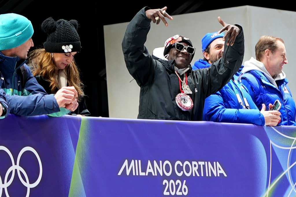 American rapper Flavor Flav, center, attends the skeleton mixed team competition at the 2026 Winter Olympics, in Cortina d&amp;apos;Ampezzo, Italy, Sunday, Feb. 15, 2026. (AP Photo/Akmal Rajput)