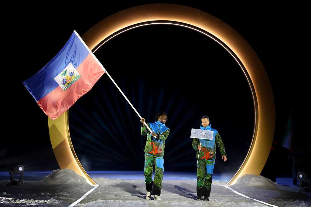 VAL DI FIEMME, ITALY - FEBRUARY 06: Flagbearer Stevenson Savart of Team Haiti enters with his teammate into the stadium during the opening ceremony of the Milano Cortina 2026 Winter Olympics at Predazzo Ski Jumping Stadium on February 06, 2026 in Val di Fiemme, Italy. (Photo by Maddie Meyer/Getty Images)