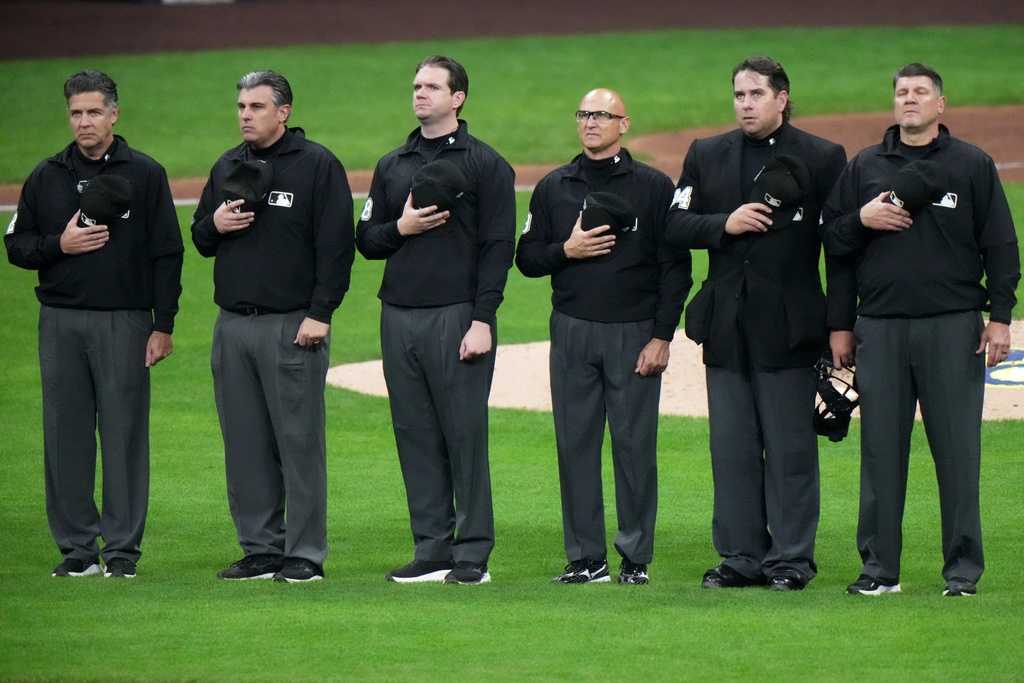 The umpire crew lines up for the singing of &amp;quot;God Bless America,&amp;quot; during the seventh inning of Game 1 of baseball&amp;apos;s National League Championship Series between the Milwaukee Brewers and the Los Angeles Dodgers Monday, Oct. 13, 2025, in Milwaukee.
