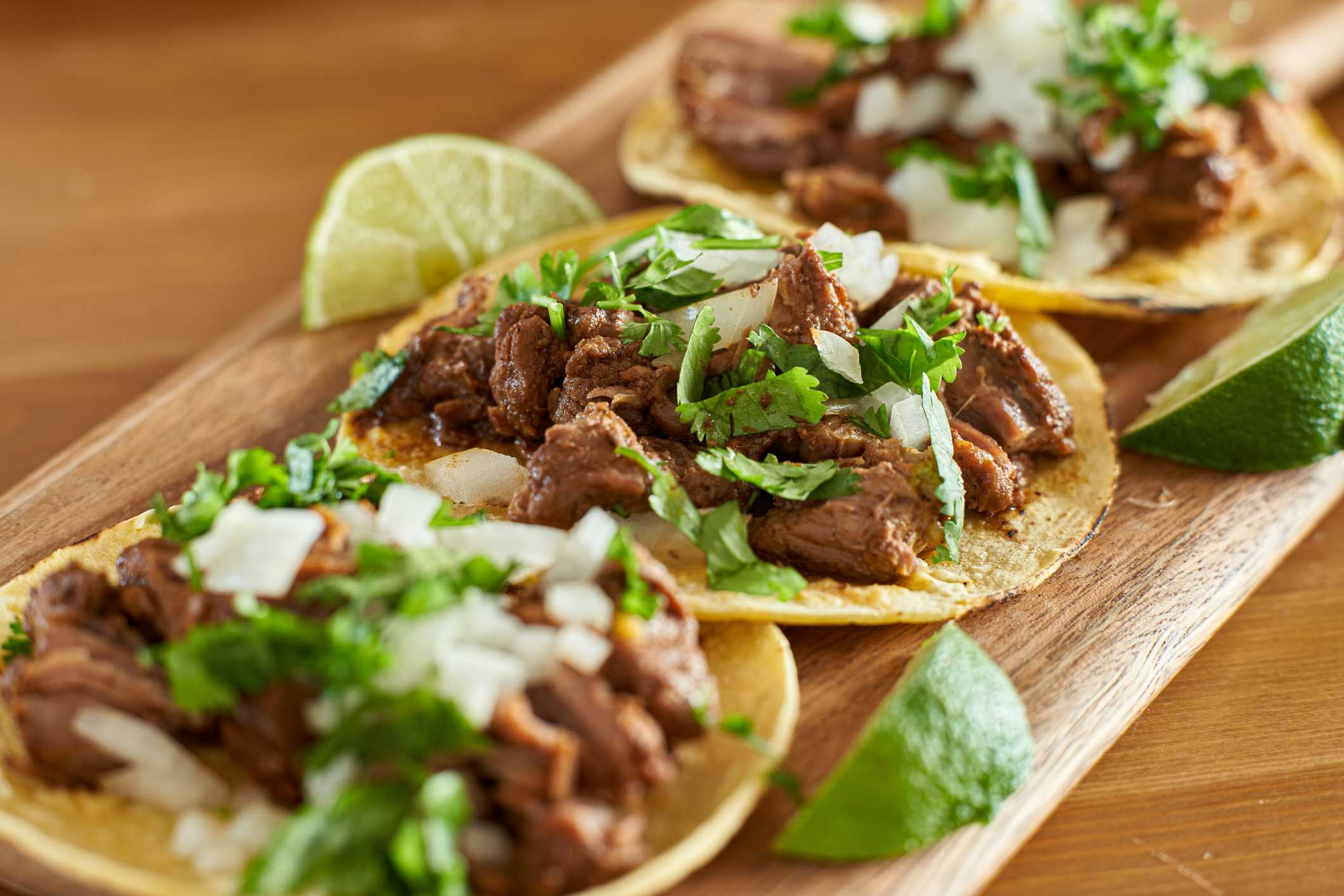 three carne asada mexican street tacos in corn tortilla with lime close up