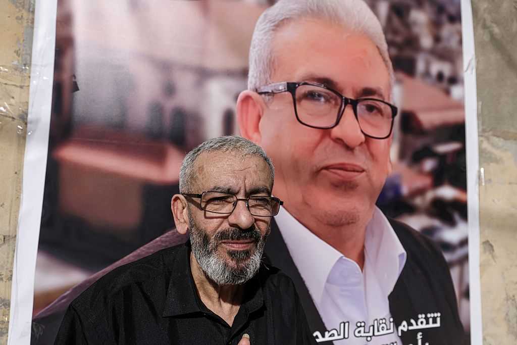 Palestinian journalist Ali al-Samoudi stands in front of a large image of himself taken before he was detained by the Israeli army and held for a year, at his home in the northern city of Jenin, in the Israeli-occupied Palestinian West Bank on May 1, 2026. Sixty-year-old Al-Samoudi was released following one-year in detention in the Israeli Naqab Prison, located in southern Israel. He was released and checked at the Jenin Hospital where he said, &amp;quot;I was 120 kilogrammes; my weight now is barely 60 kilogrammes&amp;quot;. Israel has jailed an increasing number of journalists since 2023, the year of Hamas&amp;apos;s unprecedented October 7 attack on Israel, which responded with a devastating war in the Gaza Strip. (Photo by JAAFAR ASHTIYEH / AFP via Getty Images)